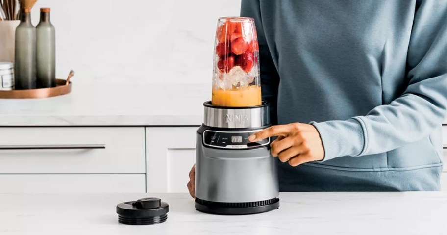 woman pushing a button on a Ninja blender filled with smoothie ingredients