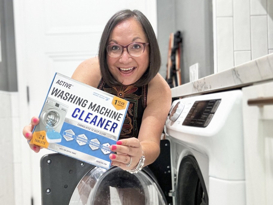 woman holding up a box of Active Washing Machine Cleaner next to washing machine