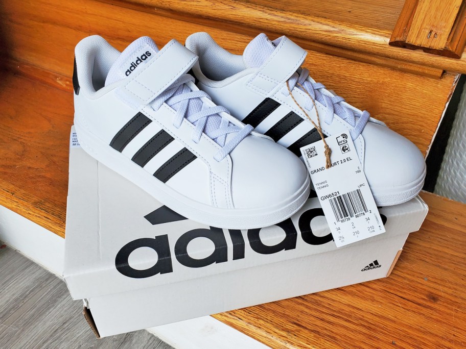 pair of white adidas sneakers with black strips on top of their shoe box