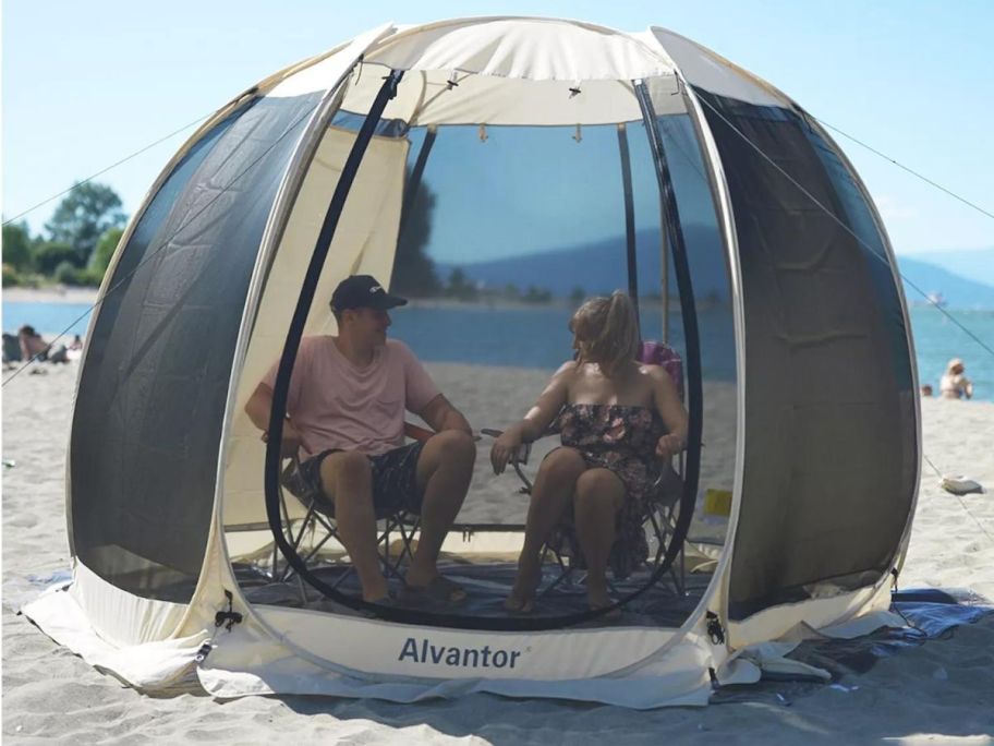 An Alvantor Pop Up Gazebo on a beach with 2 people enjoying their time inside of it