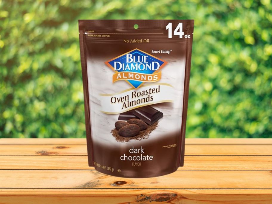 Blue Diamond Almonds Oven Roasted Dark Chocolate Flavored Snack Nuts on table with greenery behind it