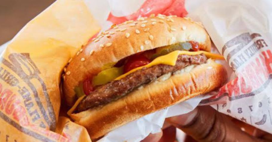 hands holding a partially unwrapped burger king cheeseburger