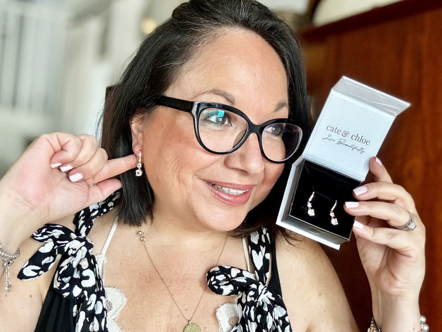 woman holding up a boxed set of earrings and touching the earring in her ear