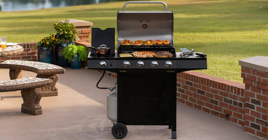 black propane grill with lid open and food cooking