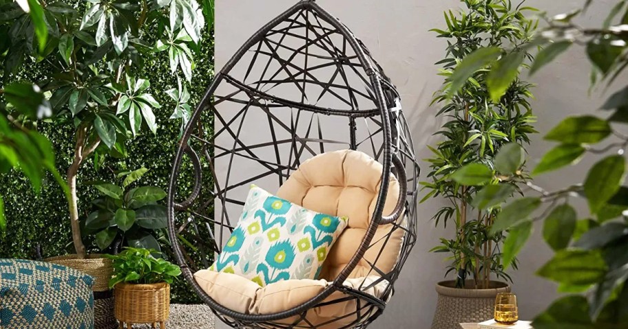 brown wicker hanging tear drop shaped chair with beige cushions and floral pillow