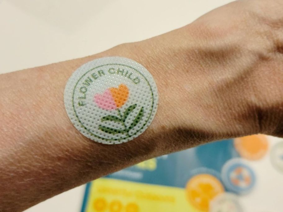 arm with a pack of Cliganic Mosquito Repellent Sticker, pack and more stickers behind it
