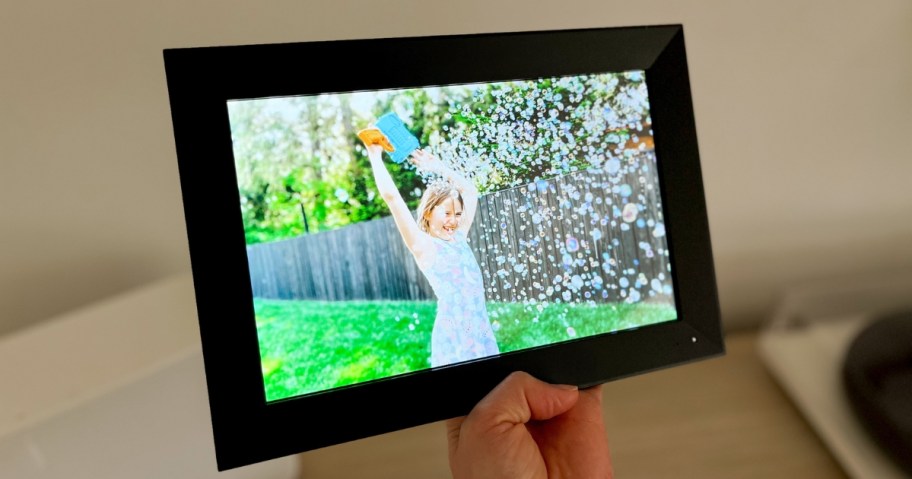 hand holding up a black digital picture frame with photo of girl surrounded by bubbles