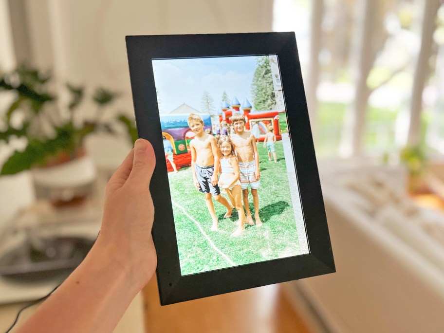 hand holding up a black digital picture frame with photo of family