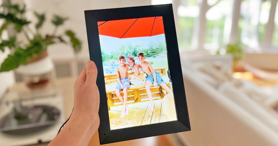 hand holding up digital picture frame with photo of kids on wood bench