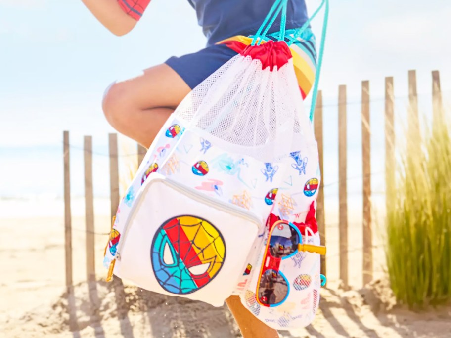 boy running on beach carrying a spider-man beach bag