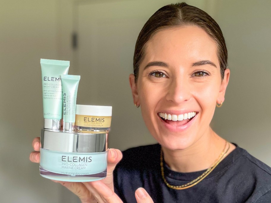 Hip Sidekick Emily Holding up an ELEMIS Super-Size Pro-Collagen Marine Cream and 3 travel size ELEMIS skincare products