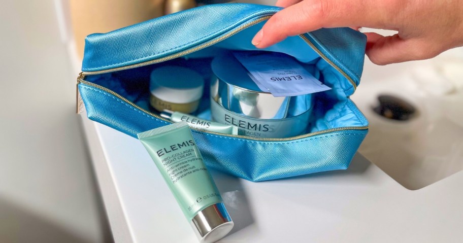 hand opening a blue cosmetic bag filled with various ELEMIS skin care items
