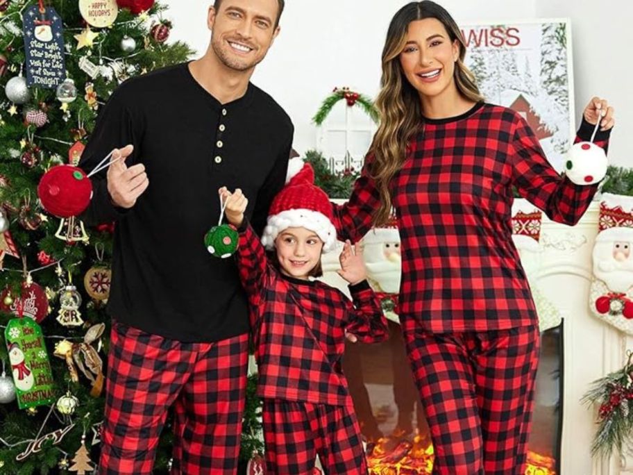 A family with a mom, dad and little girl wearing Ekouer buffalo plaid pajamas next to a Chirstmas tree