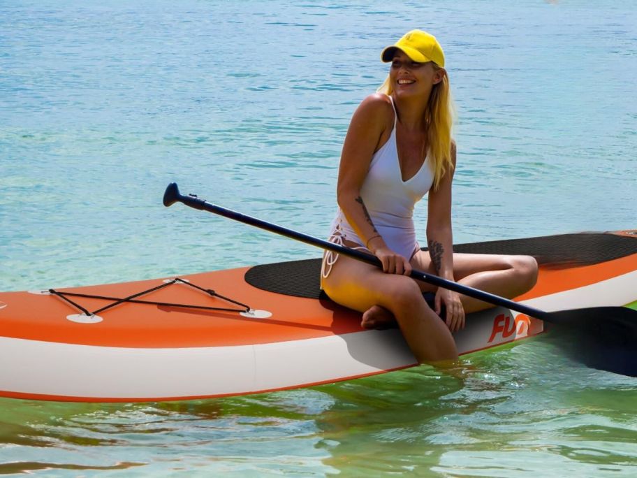A woman sitting on an orange inflatable stand up paddle board