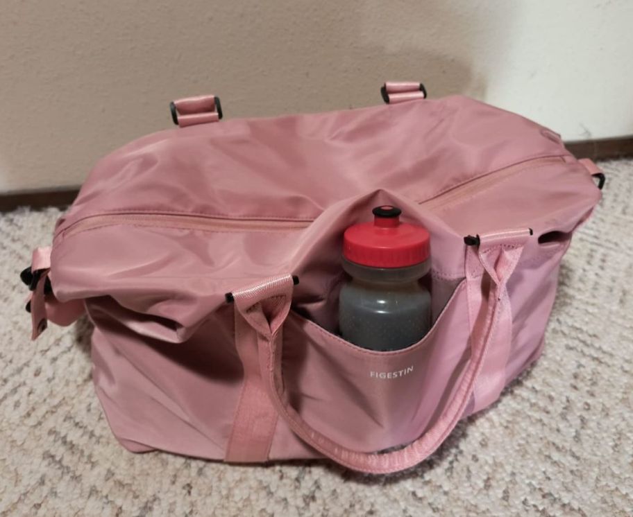 A pink weekender bag with a water bottle 