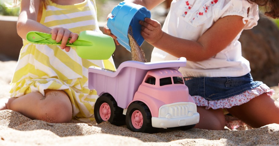 two girls putting sand into purple and pink dump truck toy
