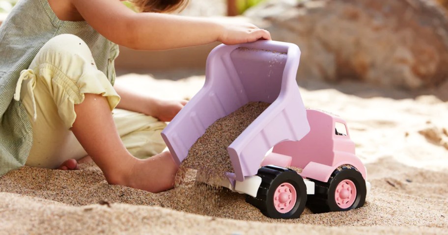 girl dumping sand out of purple and pink dump truck toy