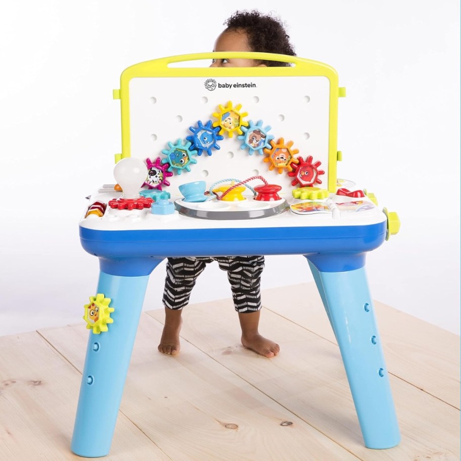 colorful baby/toddler activity table with a baby standing behind it