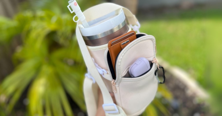 hand holding a Stanley Tumbler in a carry bag with phone and zipper pockets and strap