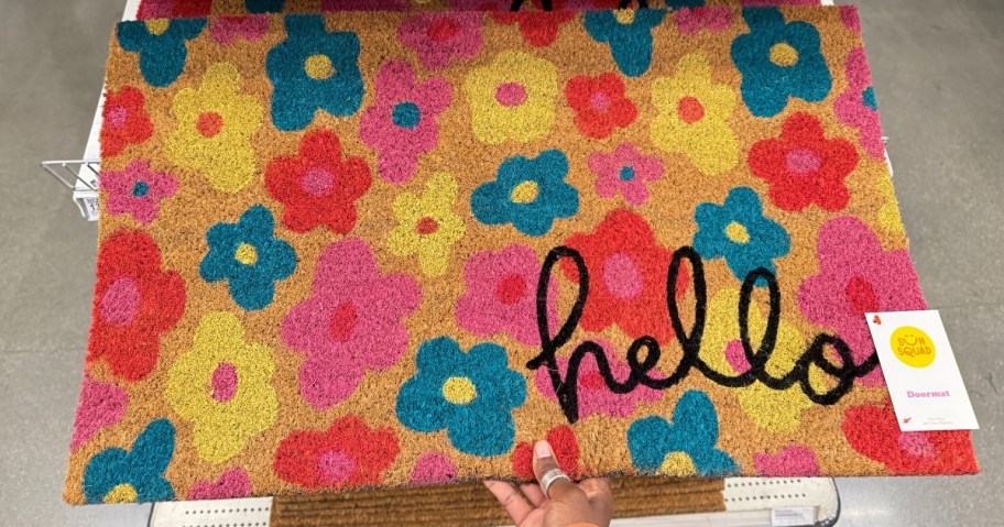 hand holding a coir doormat with pink, blue, red & yellow flowers that says "hello"