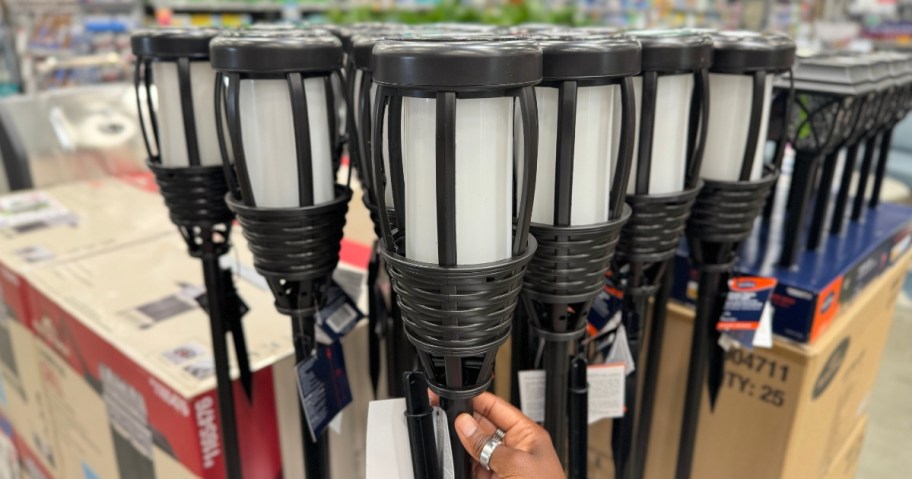 hand reaching for a solar Tiki Torch light with more behind it on display at Lowe's