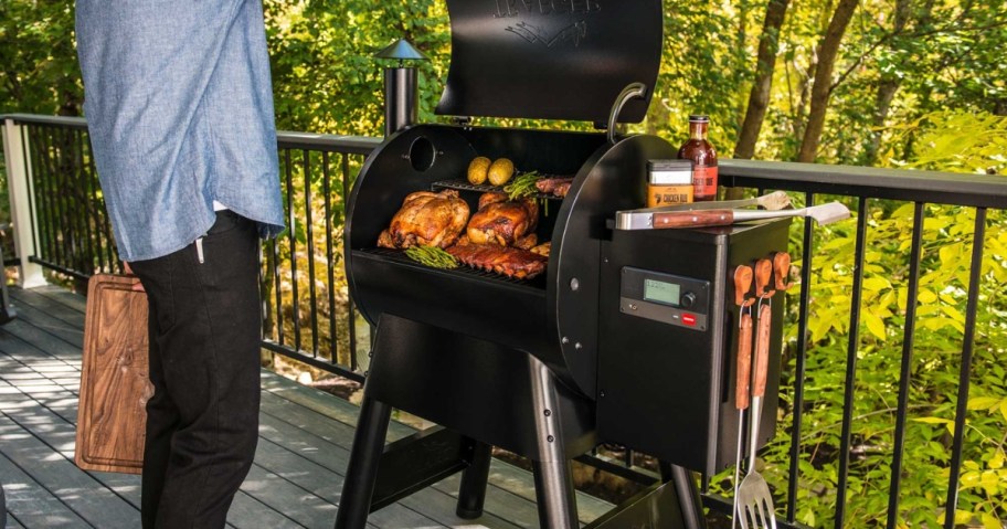 man grilling food on a large Traeger pellet grill on a back patio