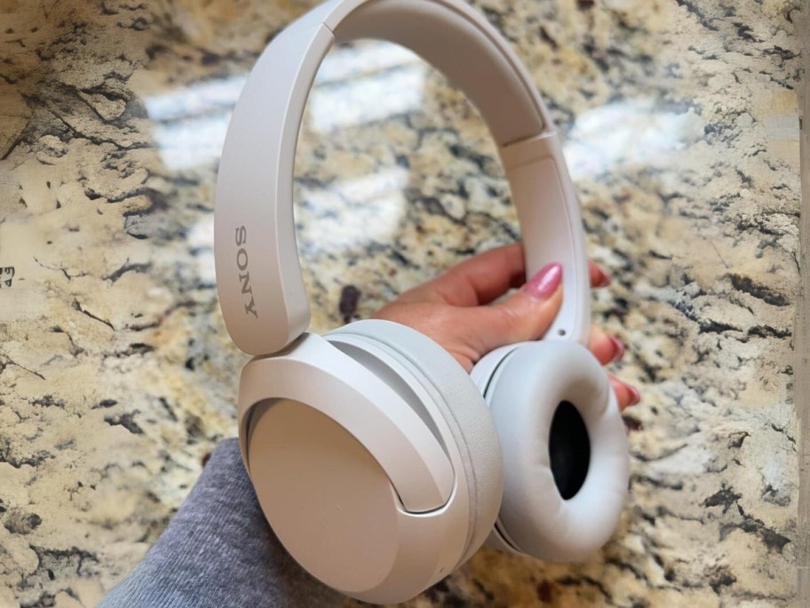 hand holding an off white Sony Wireless On-Ear Bluetooth Headset with a granite counter behind it