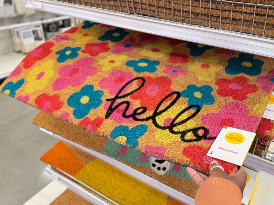 hand holding a coir doormat with pink, blue, red & yellow flowers that says "hello"