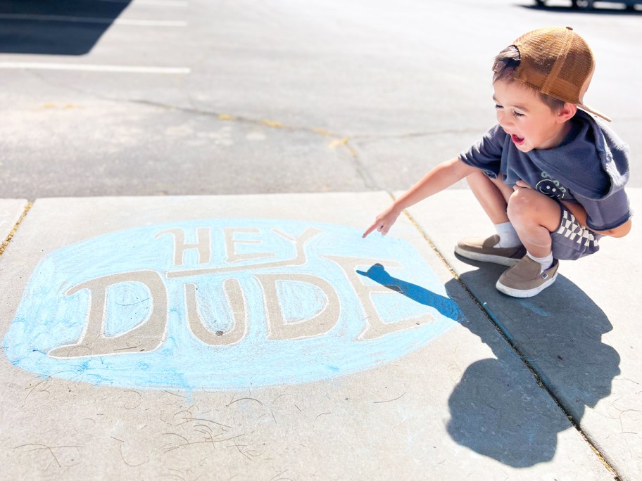 boy pointing at HEYDUDE logo in chalk on sidewalk