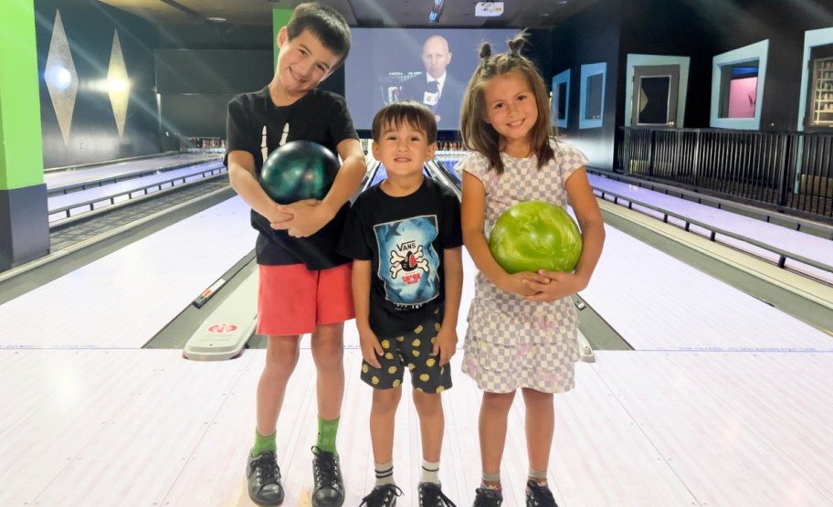 Kids standing in front of bowling aile with balls on hand