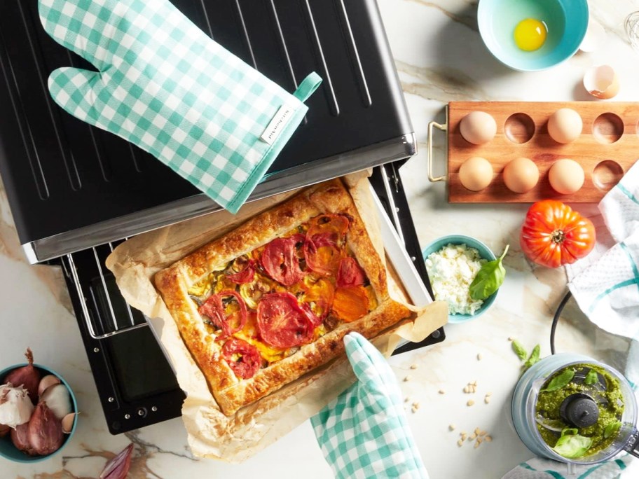using green and white gingham oven mitts to take pizza out from oven