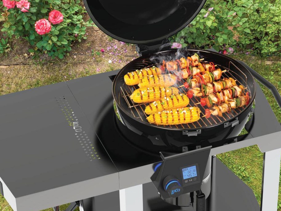 round black grill on a silver cart with kababs and corn