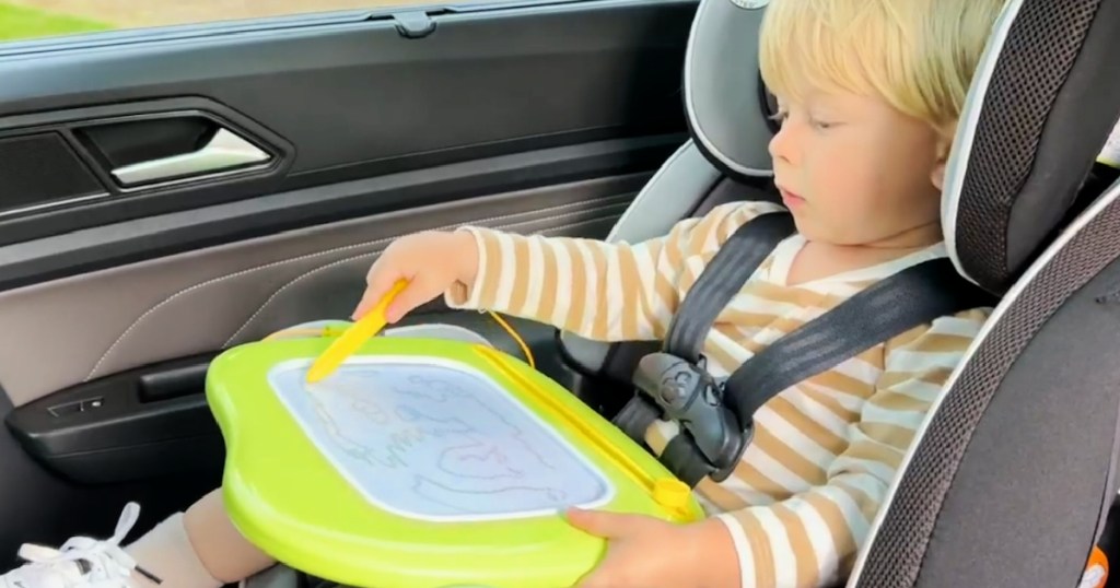 little boy in car seat drawing on magnetic board