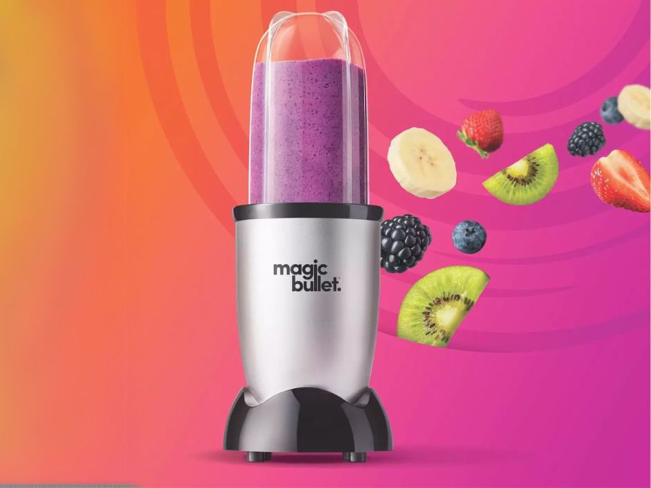 Magic Bullet Single-Serve Blender against pink and orange background with fruit next to it