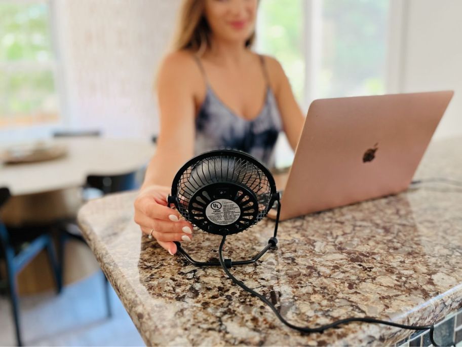 A woman working on a computer is being cooled down by a 4" personal fan. 