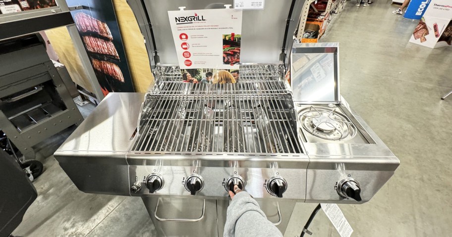 hand touching dial on silver gas grill in store