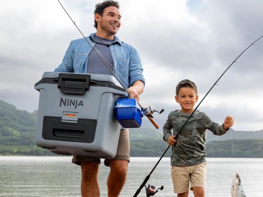 Man and little boy carrying a Ninja Frostvault cooler and fishing equipment