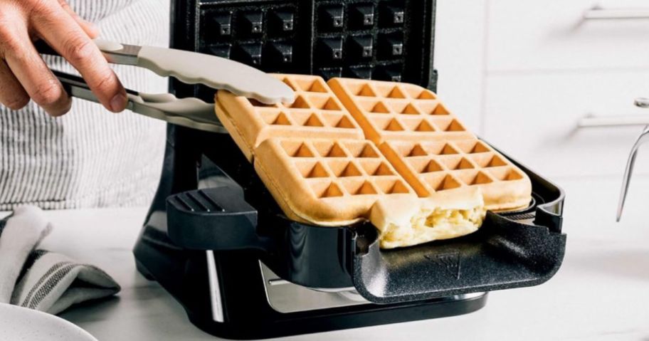 Hand taking a waffle out of the Ninja NeverStick Belgian Waffle Maker PRO with tongs