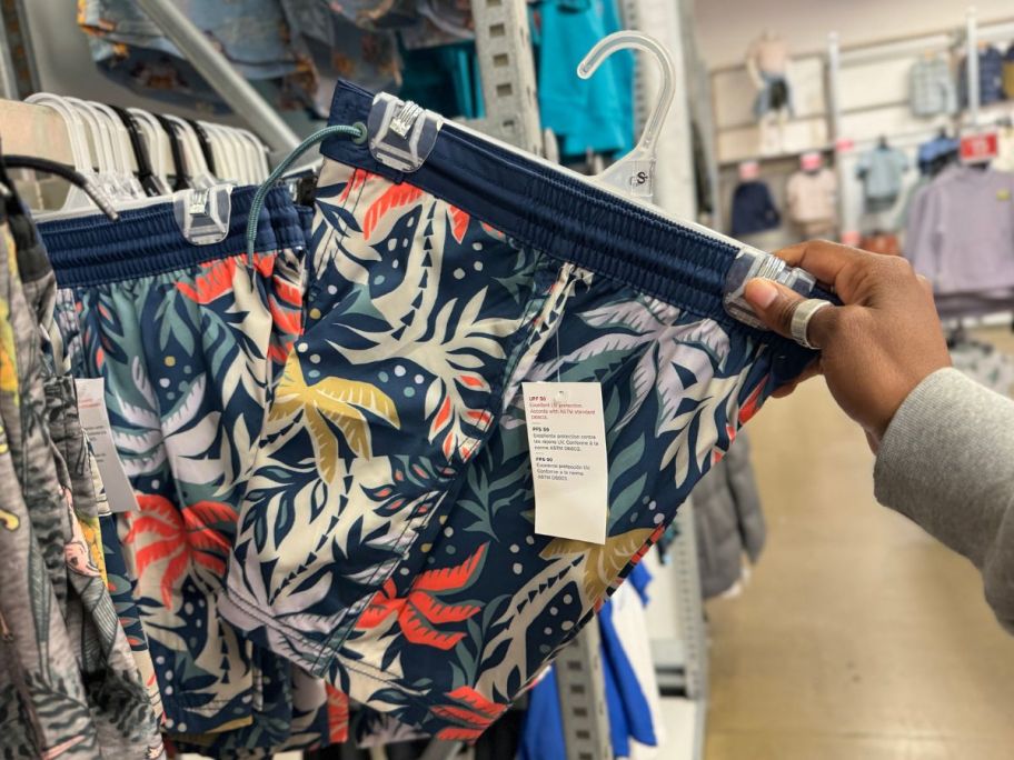 Hand taking a pair of Old Navy Boys swim trunks from the shelf
