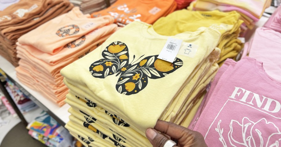 hand touching a yellow butterfly shirt on store display table