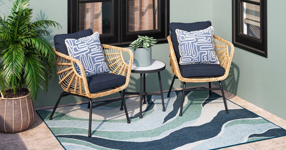 two wicker patio chairs with navy blue cushions, throw pillows, and side table