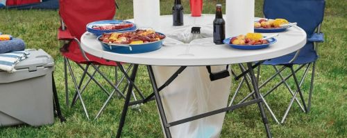 An Ozark Trail Camping table with food and drinks set on it and a trash bag hanging in the center