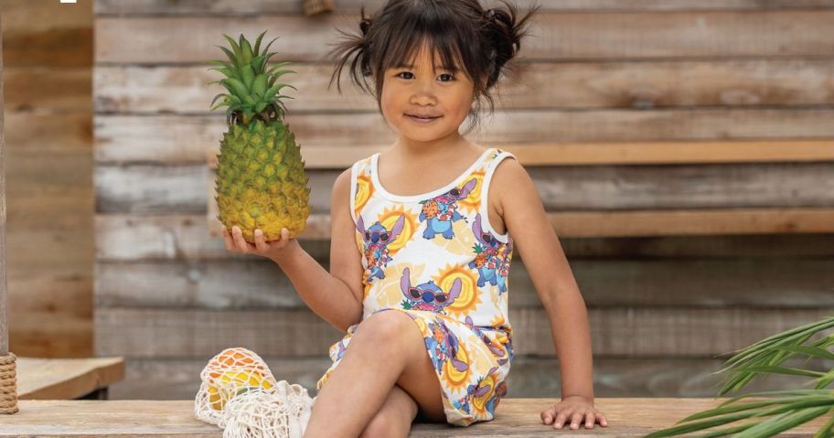 Little girl sitting holding a pineapple while wearing a Disney Stitch Sleeveless Dress from PatPat