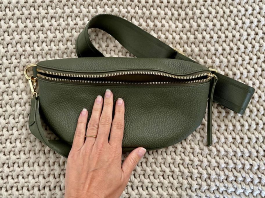 A hand touching a Quince Italian Pebbled Leather Sling Bag in Green