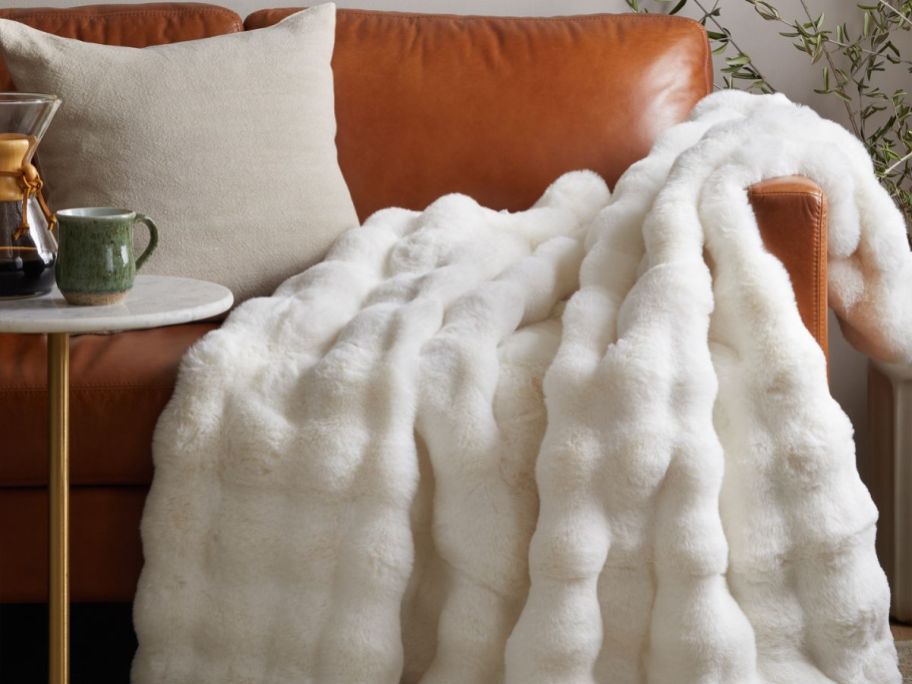 A white Quince lux throw draped over a tan leather couch