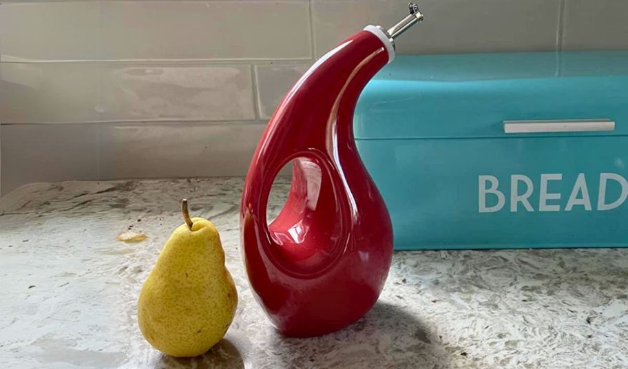 a burgundy decorative olive oil dispenser bottle on a kitchen counter next to a pear