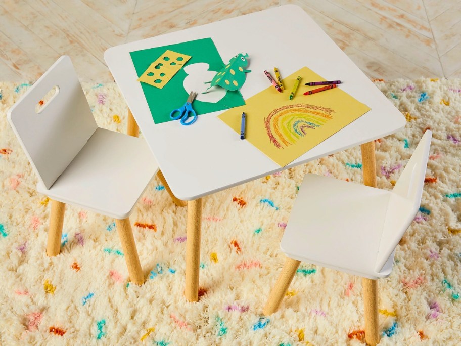 white and wood kid's activity table and chairs in a playroom with crayons and drawings on it