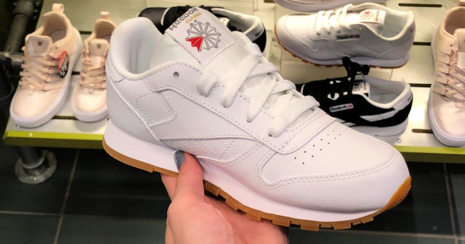 person holding up white Reebok Classic Leather Shoes