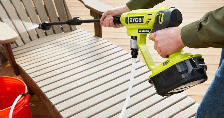 person using a yellow Ryobi pressure washer to clean a deck chair