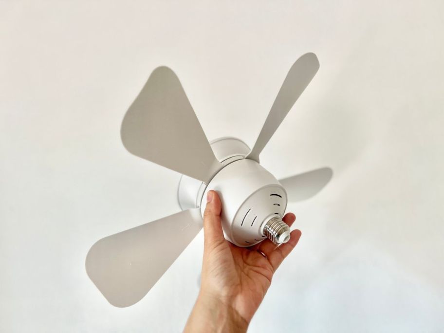 A hand holding a Socket Fan for the ceiling with a remote